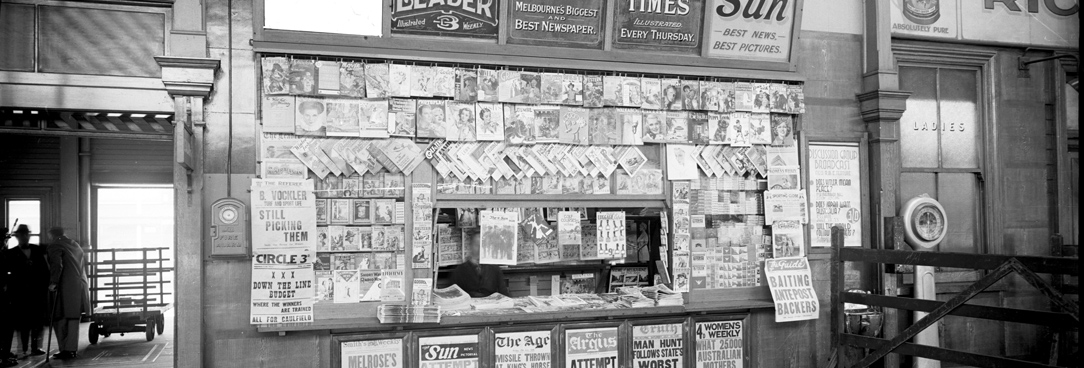 Spencer Street main concourse newspaper kiosk with painted signs for The Age, The Sun, The Weekly Times and The Herald. 18TH July 1936. VPRS 12800/ P3 item ADV 1151 Spencer Street main concourse newspaper kiosk with painted signs for The Age, The Sun, The Weekly Times and The Herald. 18TH July 1936. VPRS 12800/ P3 item ADV 1151